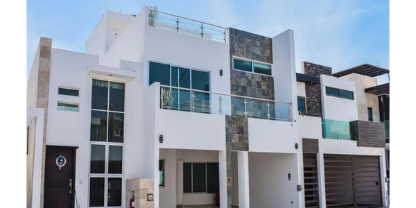 Modern white house with glass balconies and stone accents under a clear blue sky.