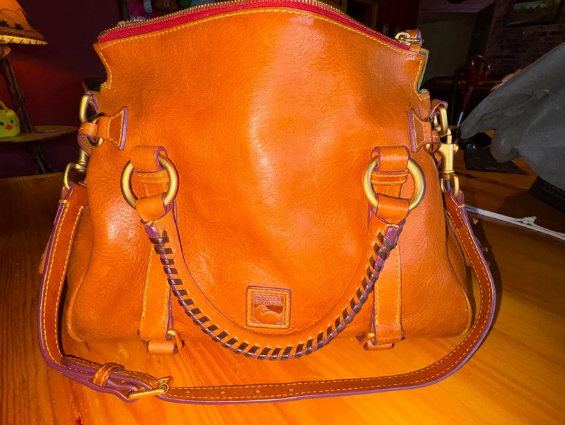 Orange leather handbag with gold hardware on a wooden table.