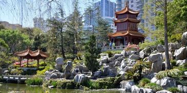 Traditional Chinese garden with pavilion and pond in urban setting.