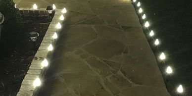 Pathway illuminated by small garden lights along its edges at night.