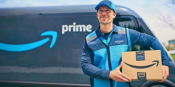 Amazon Prime delivery person holding a package in front of a branded van.