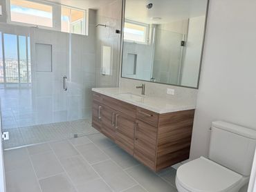 Modern bathroom with glass shower, wooden vanity, and white toilet.