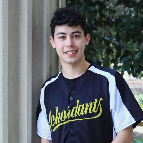Young man smiling outdoors in a black and white sports jersey.