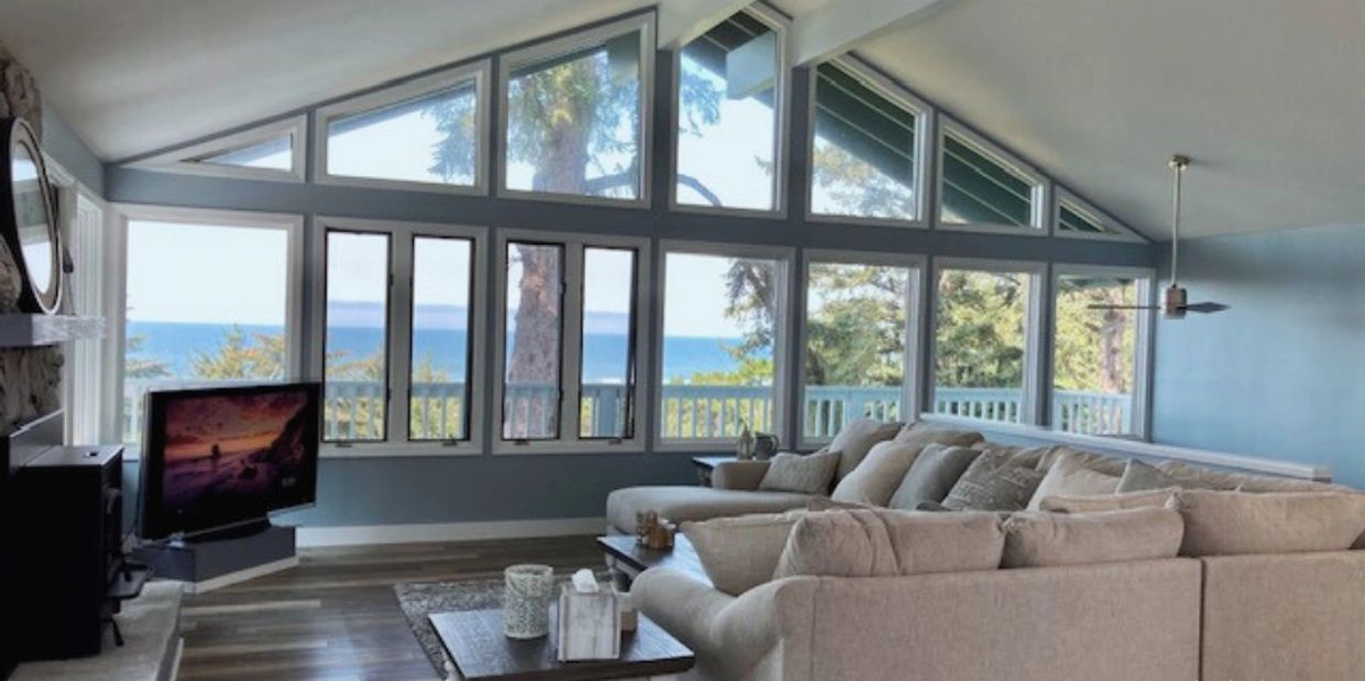 Cozy living room with large windows overlooking the ocean and trees.