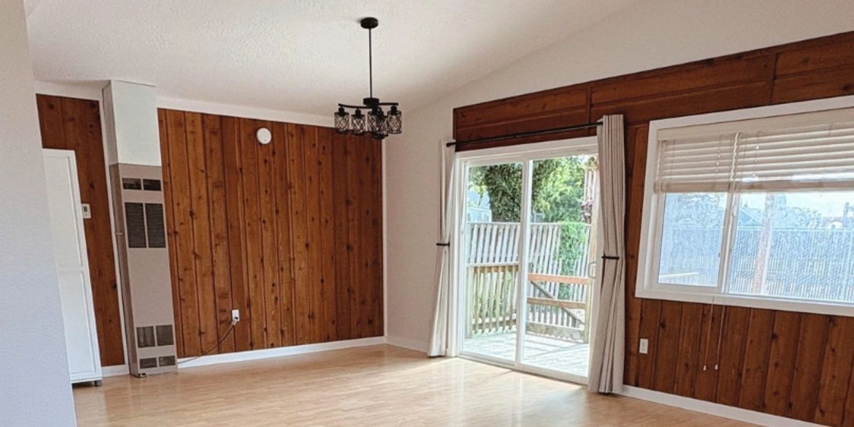 Empty room with wood-paneled walls and sliding glass door to a deck.