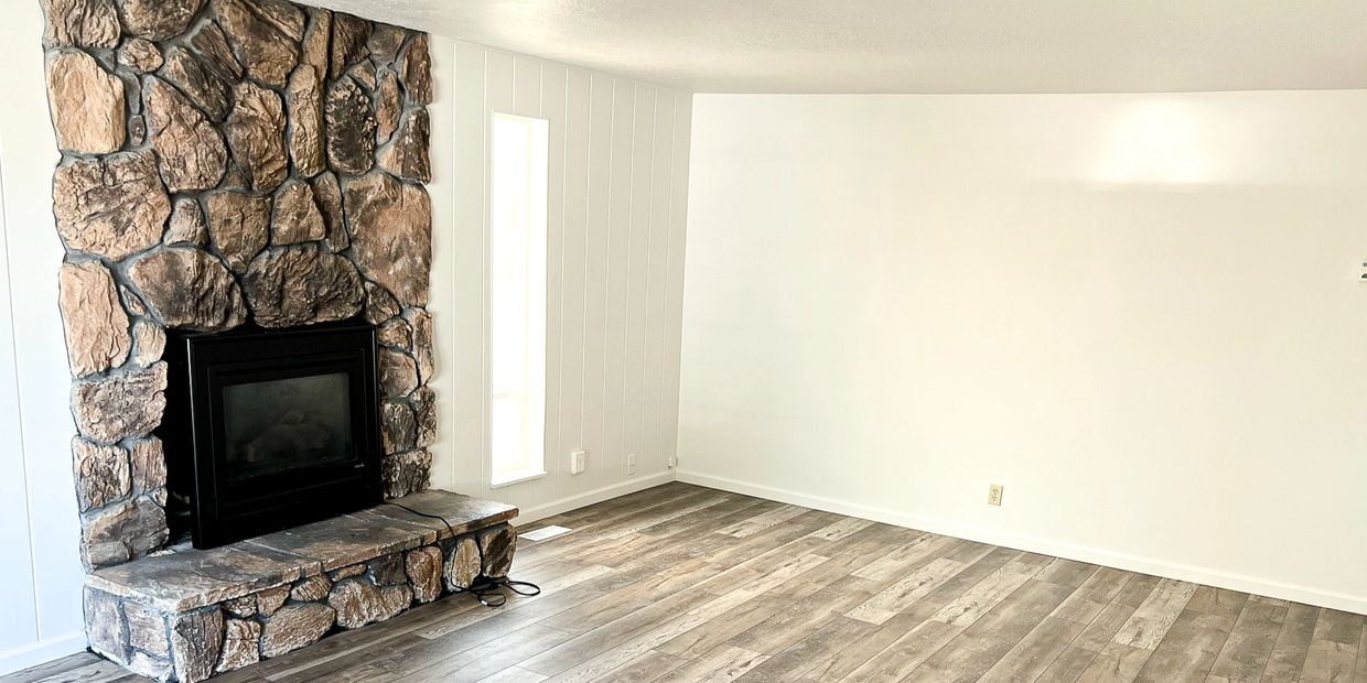 Empty room with stone fireplace and wood flooring.