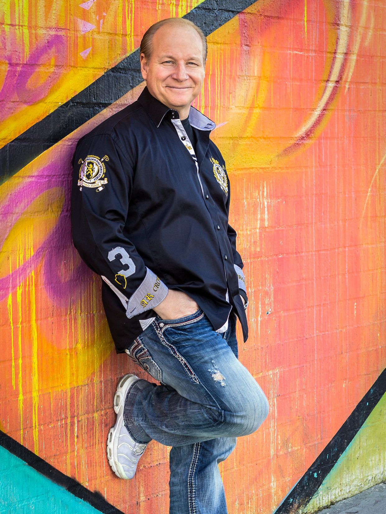 Person leaning against a colorful graffiti wall with hands in pockets.