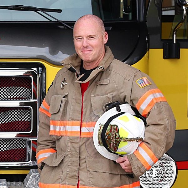 Firefighter in uniform with helmet stands by fire truck.