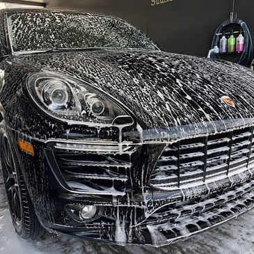 Black Porsche SUV covered in soap during a wash.