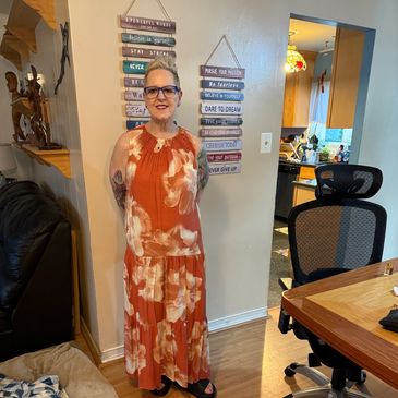 Woman in a floral orange dress standing indoors near motivational signs.