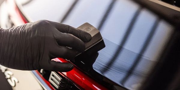 Gloved hand polishing a shiny black and red car surface.
