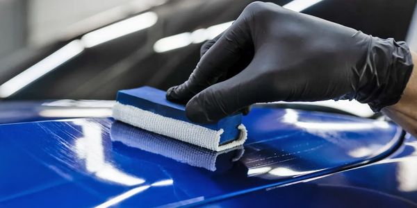 Gloved hand polishing a shiny blue car surface with a sponge.