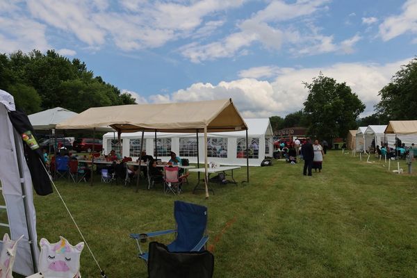Outdoor event with tents and people seated under canopies on a grassy field.