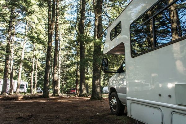 A white RV parked in a forested campground with tall trees around.