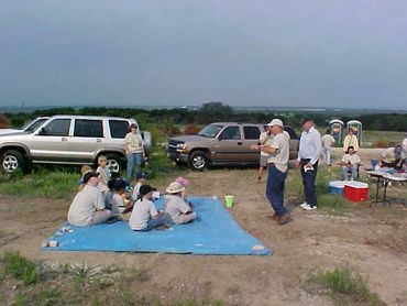 Group enjoying a picnic in an open field with parked cars.