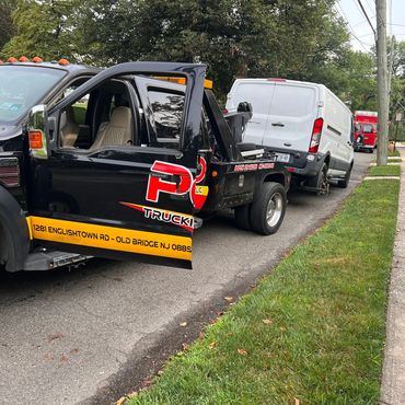 Tow truck loading a white van with missing wheels on a suburban street.