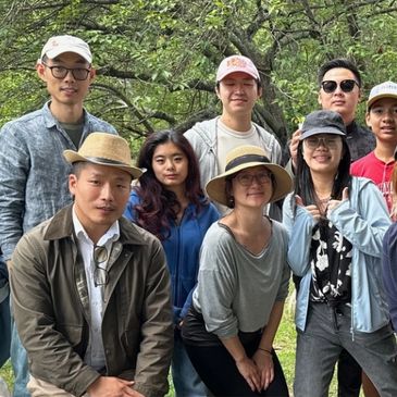 Group of friends posing outdoors with trees in background.