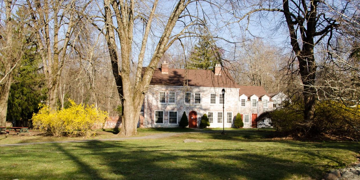 A large white brick house with red doors surrounded by bare trees and green grass.