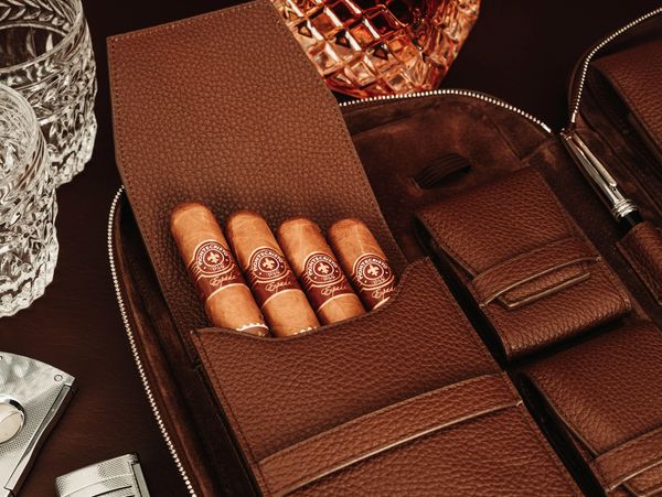 Four cigars in cigar case sitting on a table with a decanter of scotch, two rocks glasses and cutter