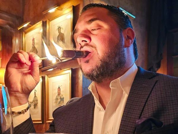 Guy sitting at a table in a cigar bar, lighting a cigar with a match flame