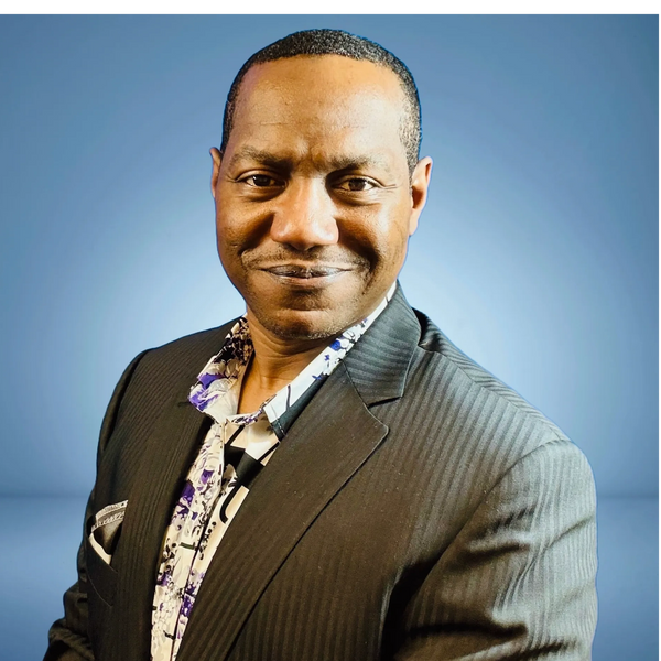 Confident man in a pinstripe suit with a floral shirt against a blue background.