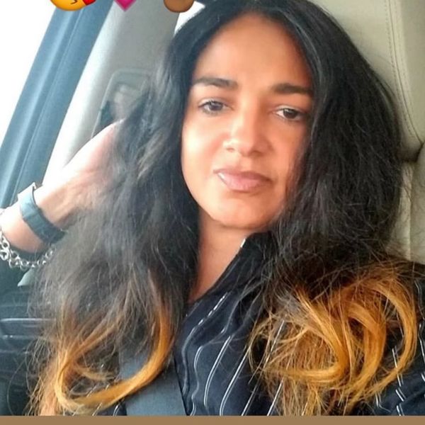 Woman with long black and brown hair sitting in a car, looking at the camera.
