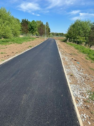 Newly paved asphalt road surrounded by greenery on a sunny day.