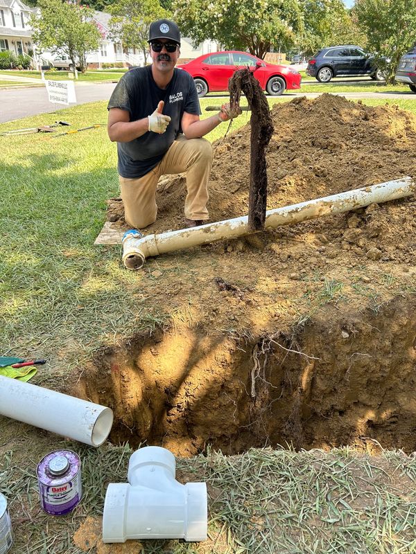 Balos Plumbing plumber digging a ditch to  replace main sewer line. Plumber holds ball of roots.