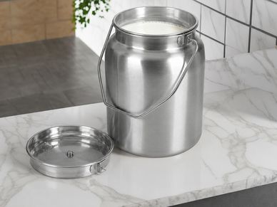 Steel container filled with milk on a marble counter.