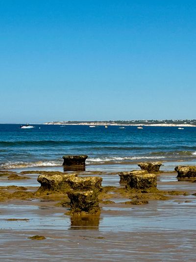 Rock formations on a beach with boats in the distance.