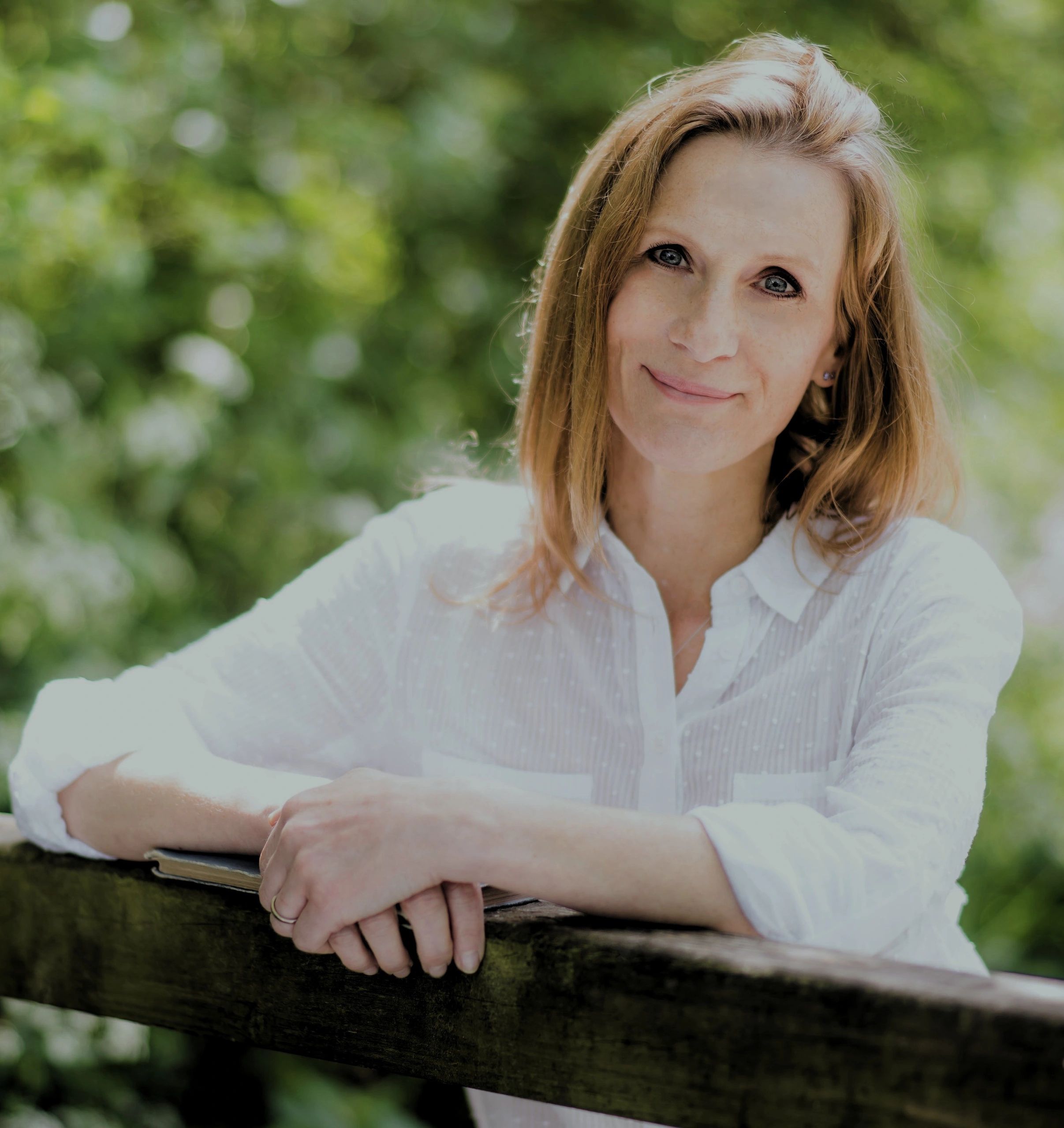 Smiling woman with red hair leans on wooden railing outdoors.
