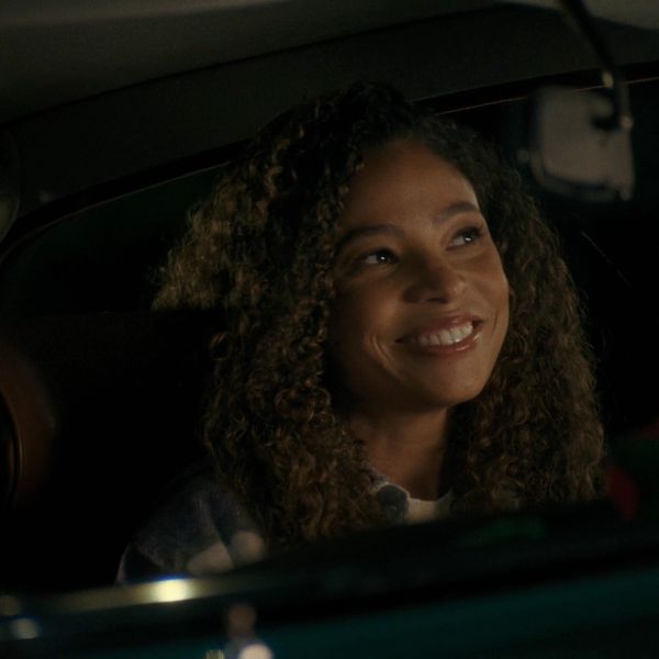 A woman with curly hair smiling inside a car at night.