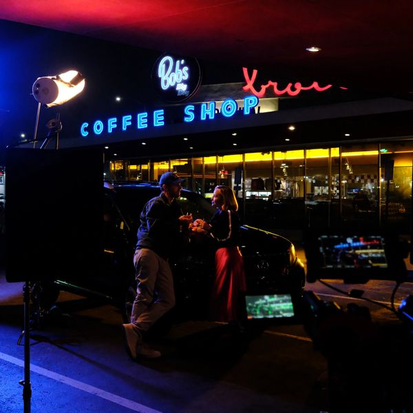 Nighttime scene of two people talking outside Bob's Coffee Shop with film equipment around.