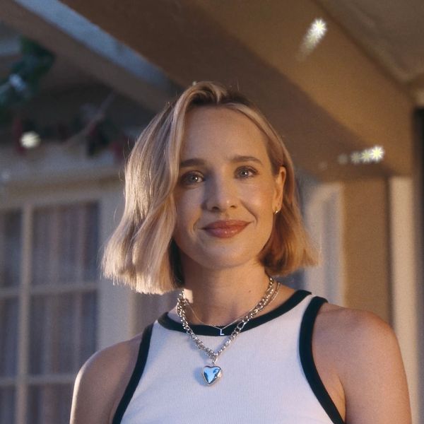 A smiling woman with short blonde hair wearing a white tank top and heart-shaped necklace.
