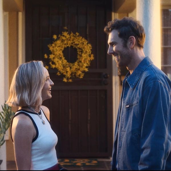 A woman and a man smiling at each other in front of a door with a yellow wreath.