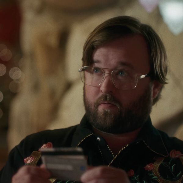 Man with glasses and beard holding a card, looking contemplative.