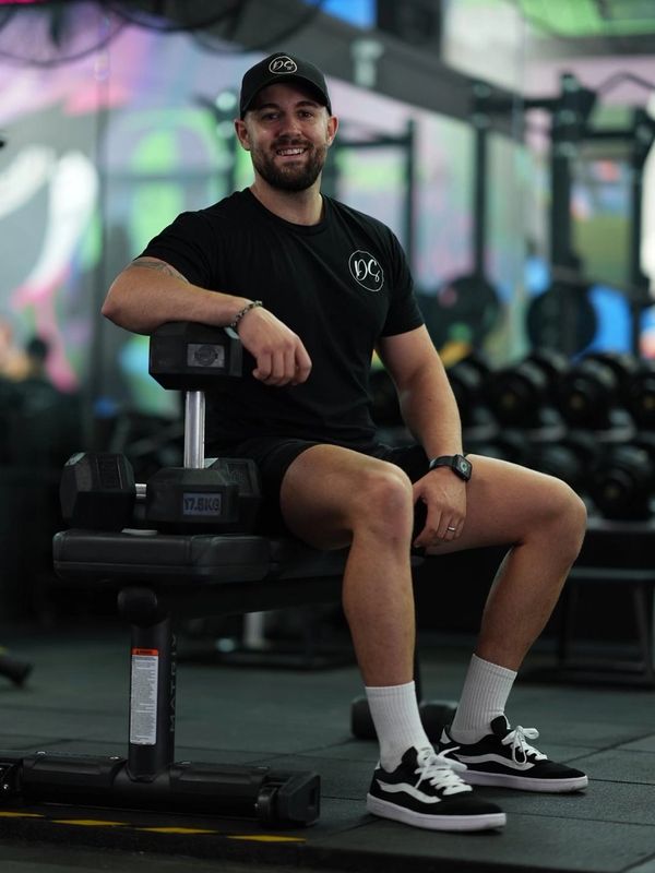 welcoming photo of a nutritionist leaning on a dumbbell smiling at the camera 