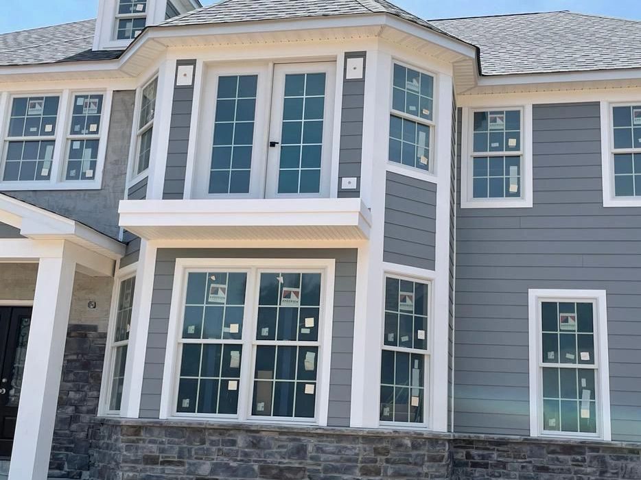 Newly constructed gray house with white trim and multiple windows under a clear blue sky.