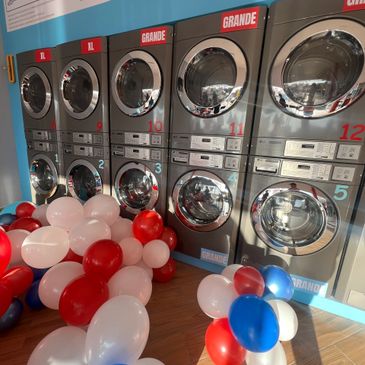 Row of washing machines with red, white, and blue balloons on the floor.