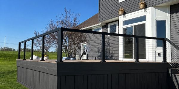 Modern wooden deck with black metal railing attached to a gray house.