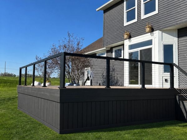 Modern elevated deck with black railing attached to a gray house.