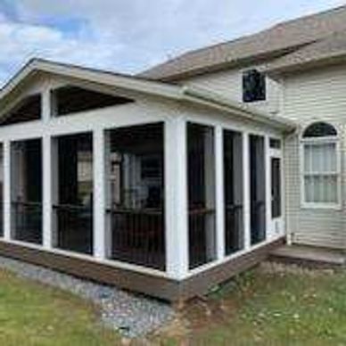 A screened porch attached to a beige house under a cloudy sky.