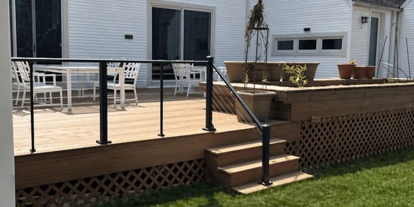 A wooden deck with a black metal railing and white outdoor chairs.