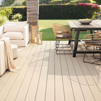 Cozy outdoor patio with wicker chairs, a wooden table, and a cushioned sofa under natural sunlight.