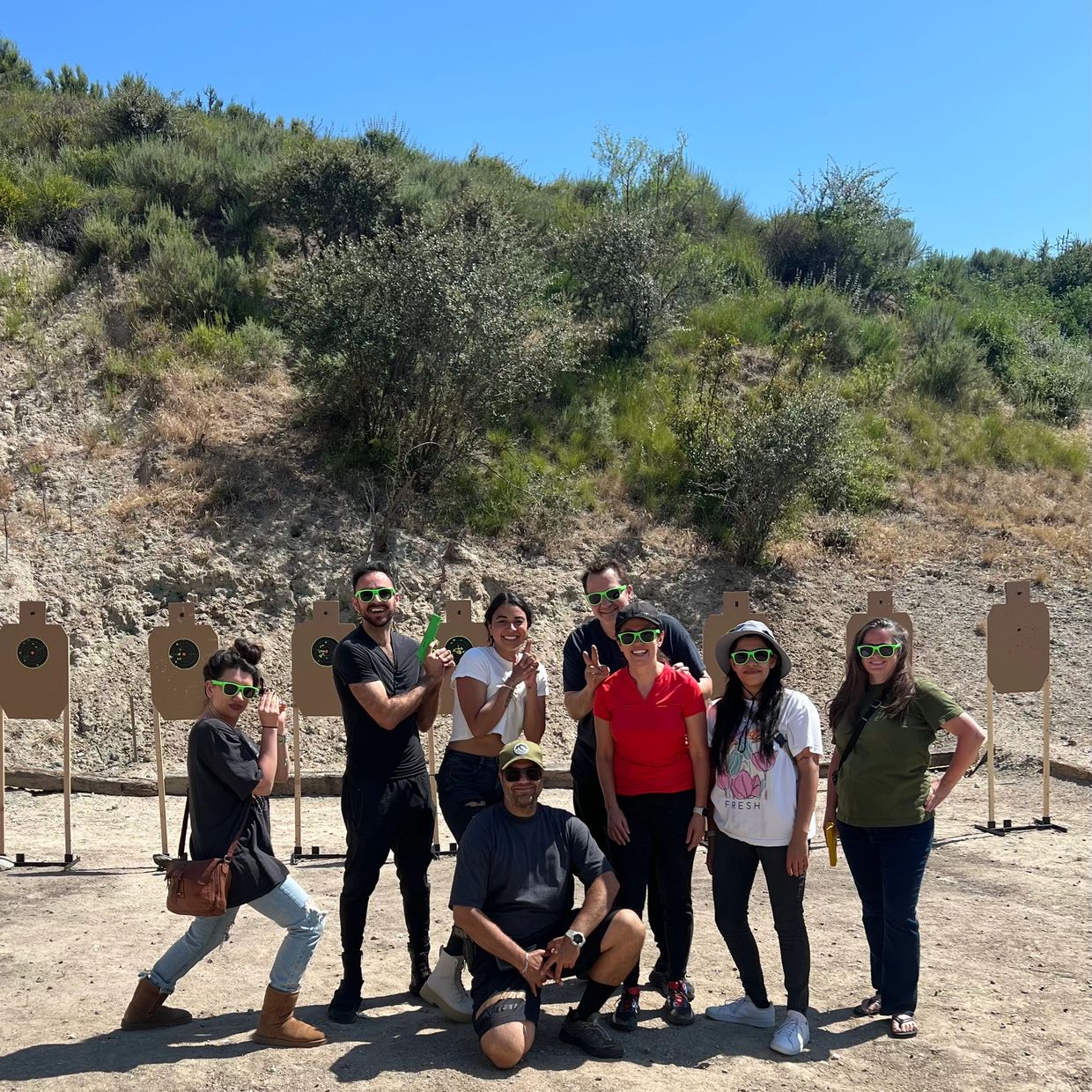 Group of people wearing green sunglasses at an outdoor shooting range.
