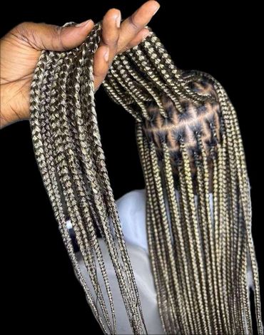 Hand holding long, neatly braided blonde and brown hair against a black background.