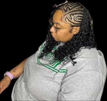 Woman with intricate braided and curly hairstyle wearing glasses and a grey shirt.