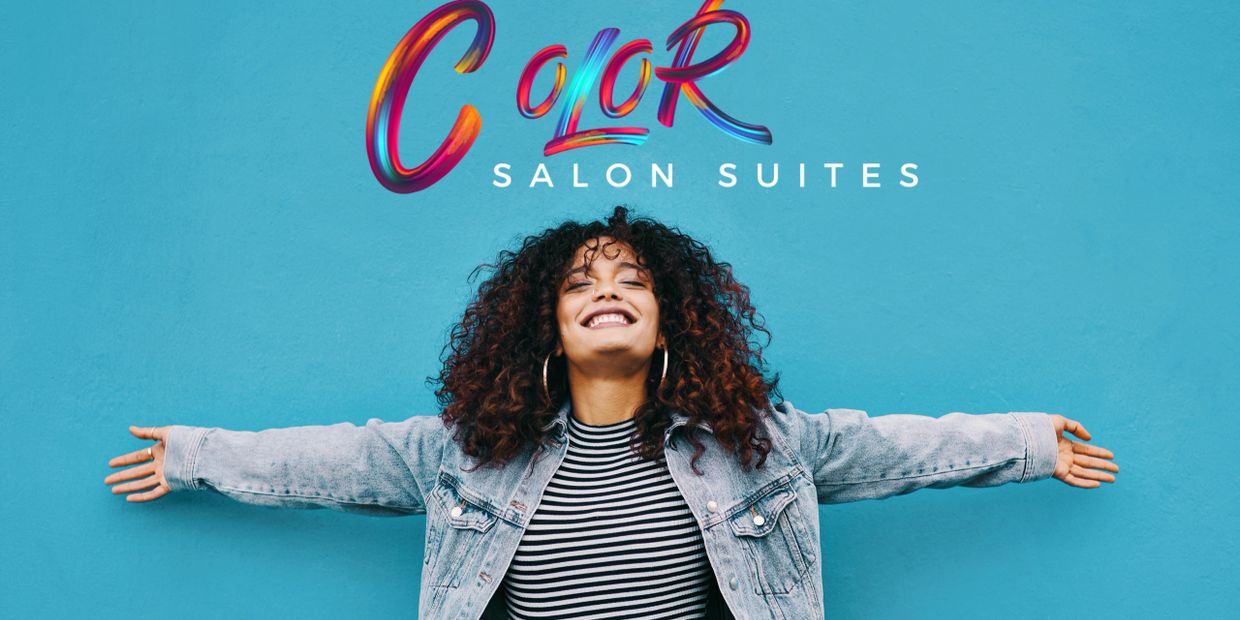 A woman smiling with open arms in the background of a Color Salon Suites sign.