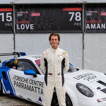 Young race car driver stands confidently in front of a Porsche race car.
