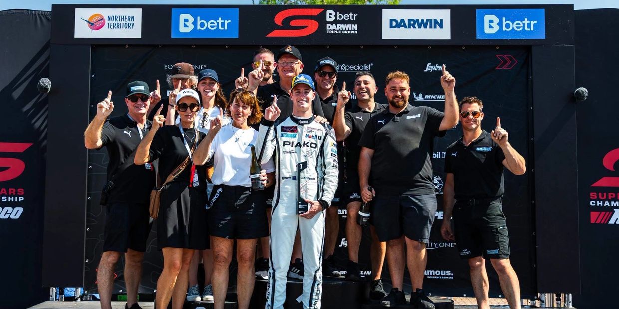 Race team celebrating a victory with champagne and trophies.